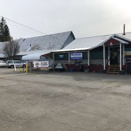 A small commercial building with a covered entrance, featuring a sign that reads "The Pigeon and The Poutiner." There are parked vehicles in front, and another building is visible in the background.