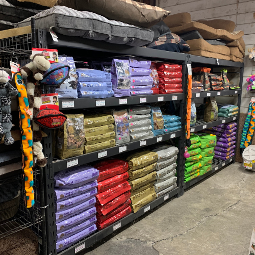 A store shelf stocked with various pet food bags in different colors and brands, along with toys and accessories displayed on the side.