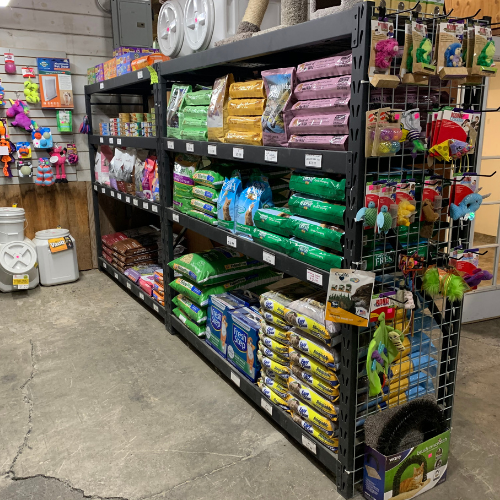 A store aisle with shelves filled with various bags of pet food and supplies, alongside colorful pet toys.